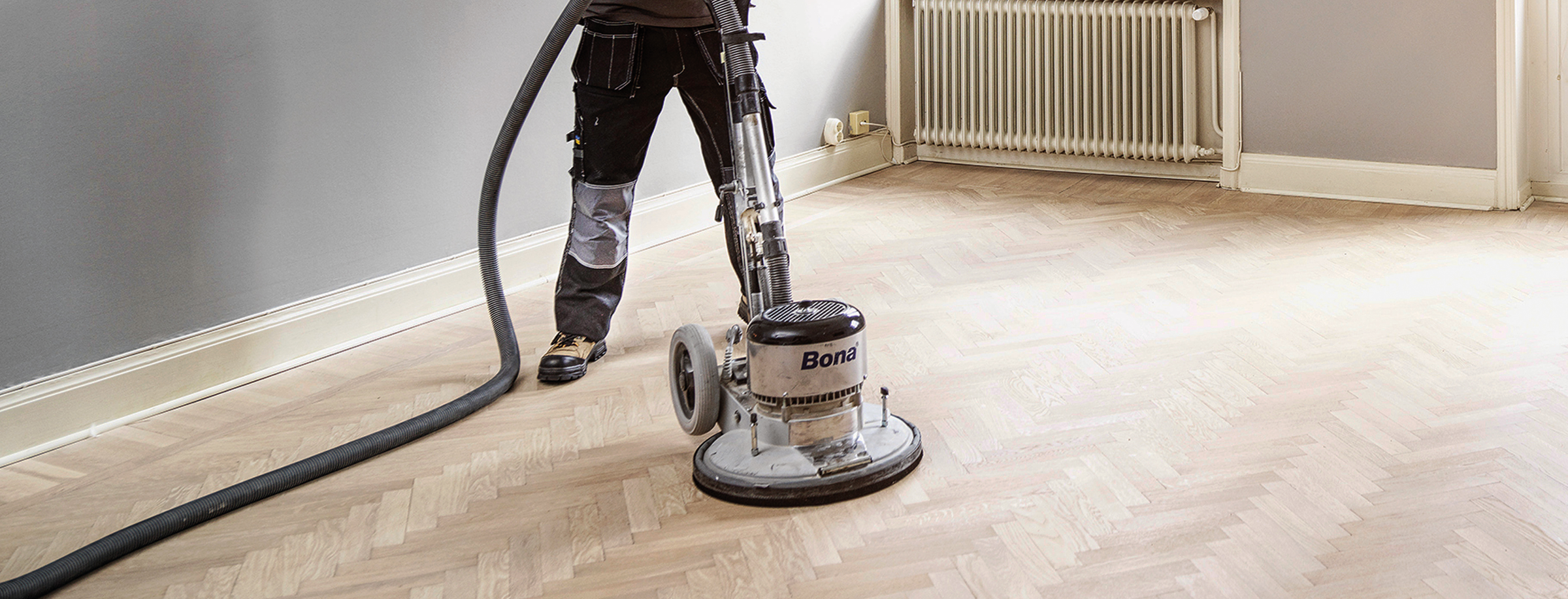A flooring professional is using a Bona Power Drive on a hardwood floor, sanding it to an execeptionally, smooth texture.