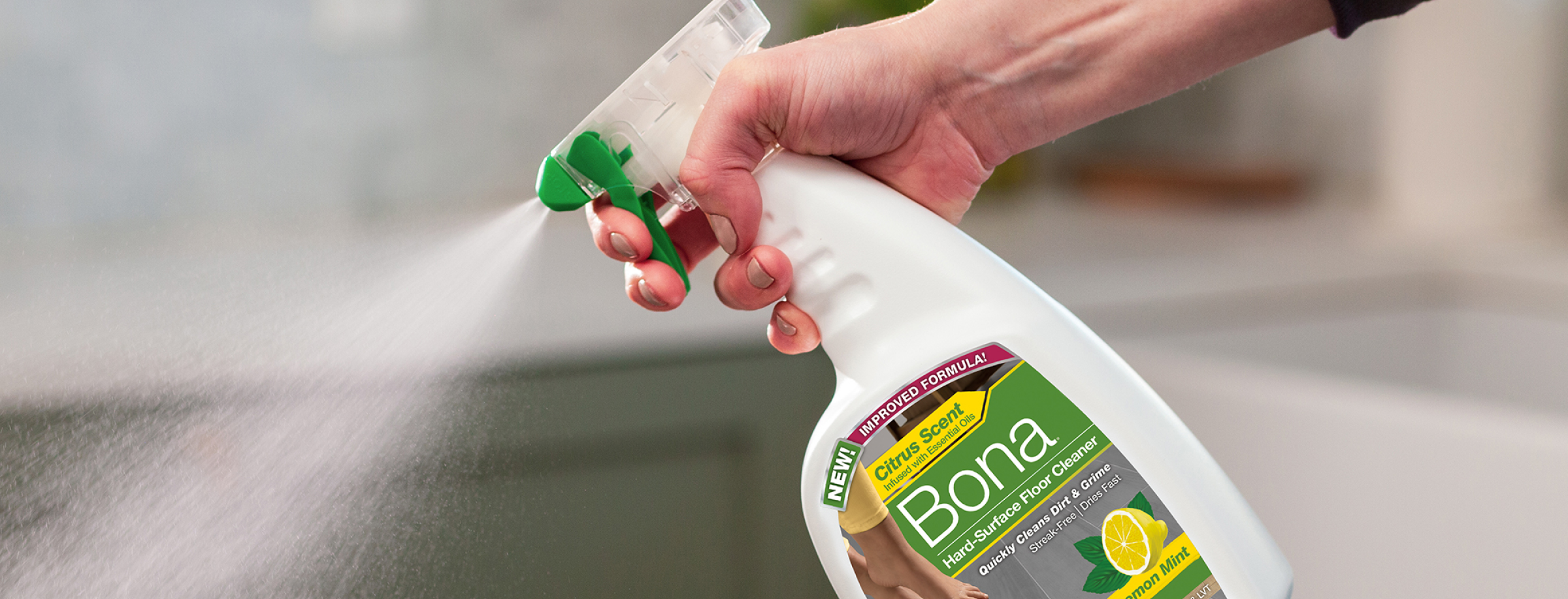 A hand sprays Bona Hard-Surface Floor Cleaner Lemon Mint scent onto a bathroom floor.