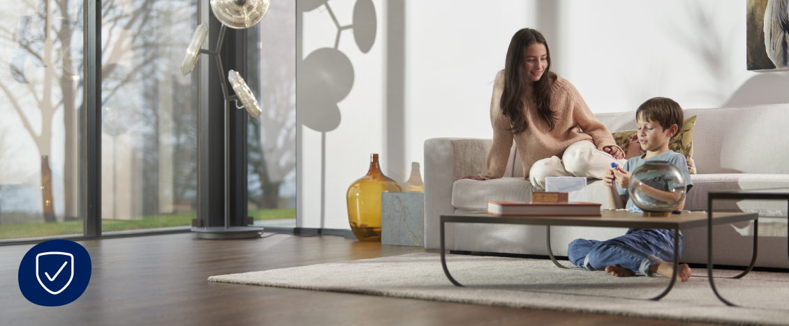 A woman sits on a sofa with a boy in a sunlit living room featuring Bona clean hard-surface floors.